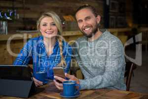 Portrait of smiling couple with coffee and technologies in cafe