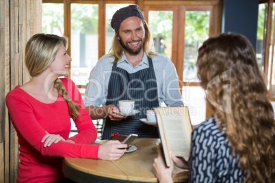 Smiling barista serving coffee to female customers in cafe