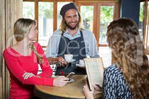 Smiling barista serving coffee to female customers in cafe