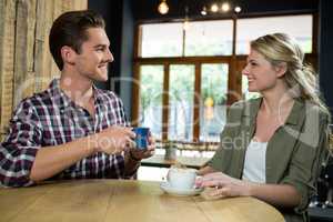 Smiling couple talking while having coffee at table in cafeteria