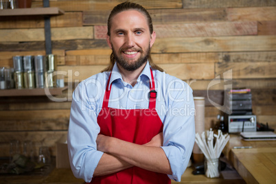 Smiling male barista standing arms crossed in cafeteria
