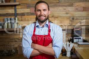 Smiling male barista standing arms crossed in cafeteria