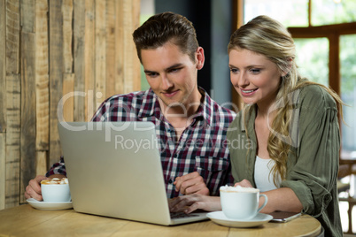 Smiling couple using laptop at table in coffee shop