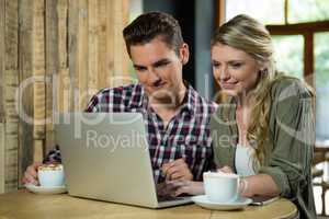 Smiling couple using laptop at table in coffee shop