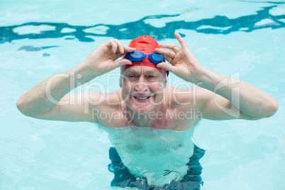 Happy senior man holding goggles in swimming pool