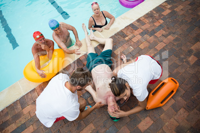 Friends looking at lifeguards saving unconscious senior man at poolside