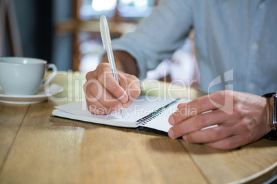 Young man writing in diary at table in coffee shop