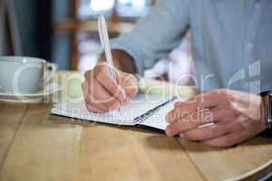 Young man writing in diary at table in coffee shop