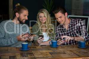 Smiling friends using smart phones at table in cafe