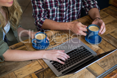 Couple using laptop while having coffee in cafeteria