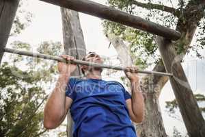 Fit man performing pull-ups on bar during obstacle course