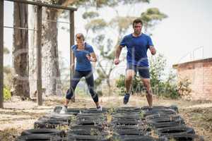 Man and woman running over the tyre during obstacle course