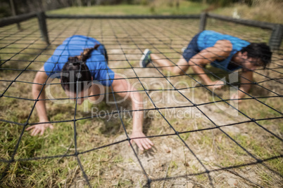 Fit man and woman crawling under the net during obstacle course