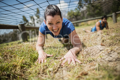 Fit woman crawling under the net during obstacle course