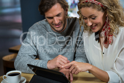 Happy couple using tablet PC at table in cafeteria