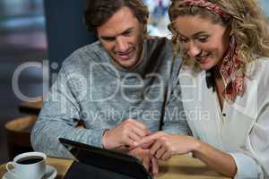 Happy couple using tablet PC at table in cafeteria