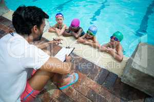 Male instructor with clipboard explaining little swimmers at pooldise