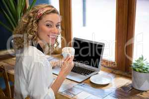 Smiling young woman having coffee while using laptop at cafe