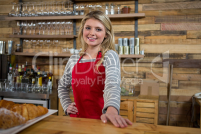 Smiling young female barista at counter in coffee shop