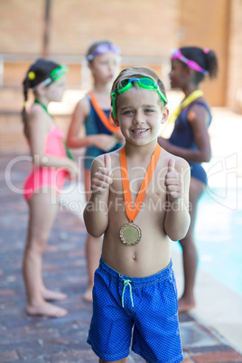 Little swimmer showing thumbs up at poolside