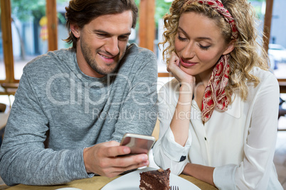 Smiling couple using smart phone at table in cafe