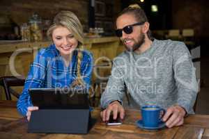 Smiling couple using tablet computer at table in cafeteria