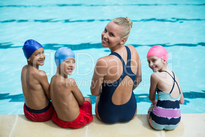 Female swimming instructor with students sitting at poolside