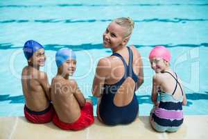 Female swimming instructor with students sitting at poolside