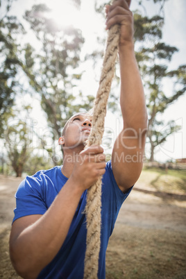 Fit man climbing rope during obstacle course