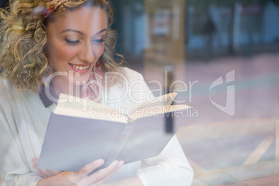 Smiling woman reading book seen through cafe window