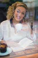 Woman having coffee while reading book seen through cafe window