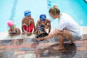 Female instructor showing clipboard to children at pool side