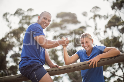 Man assisting woman to climb a hurdles during obstacle training