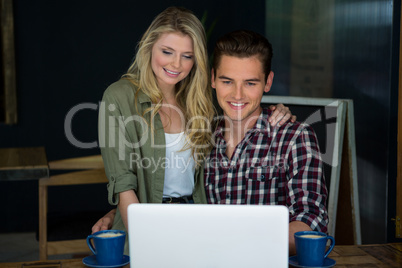 Smiling couple using laptop at table in coffee shop