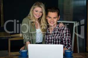 Smiling couple using laptop at table in coffee shop