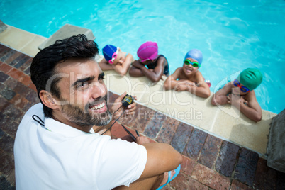 Instructor using stopwatch with little swimmers at poolside