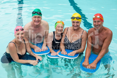 Senior swimmers posing with kickboards in pool