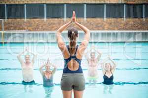 Rear view of female yoga instructor assisting senior swimmers