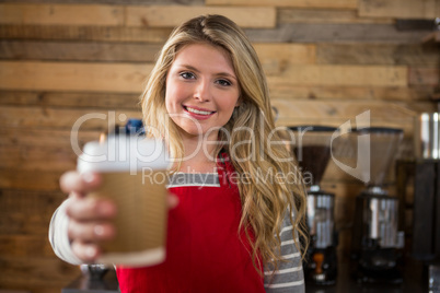 Smiling female barista holding disposable coffee cup in cafe
