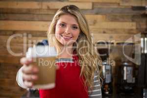 Smiling female barista holding disposable coffee cup in cafe