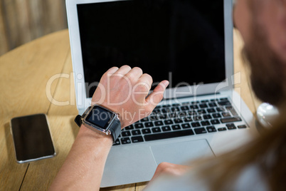 Man using smart watch with laptop and mobile phone on table in cafe