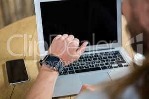 Man using smart watch with laptop and mobile phone on table in cafe