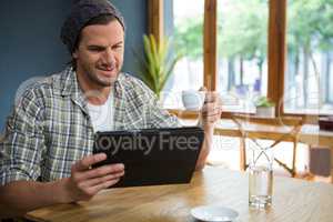Man having coffee while holding digital tablet at table in cafe