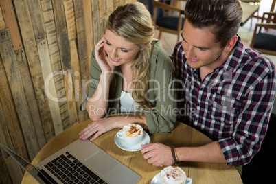 Young couple using laptop at table in coffee shop