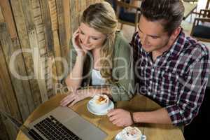 Young couple using laptop at table in coffee shop