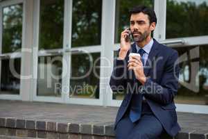 Businessman holding disposable coffee cup talking on mobile phone