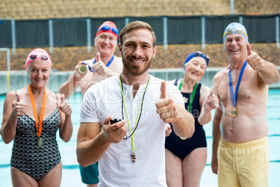 Instructor and senior swimmers showing thumbs up at poolside