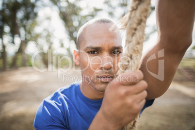 Portrait of fit man climbing rope during obstacle course