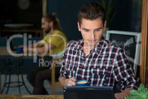 Man having coffee while using digital tablet in cafeteria