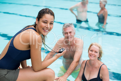 Young female trainer and senior swimmers at poolside